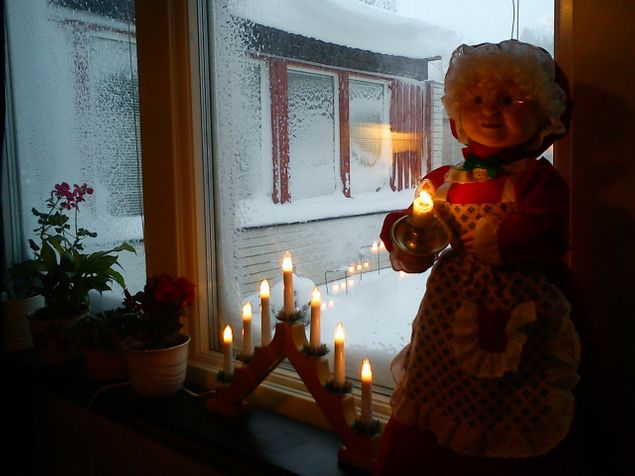 Mycket snö har det kommit!
I fönstret står tomtemor med ett tänt ljus och ljusstaken är tänd.
Adventsljusstaken kanske känns som en gammal tradition men det var först på 1920-talet som vi började tända ett ljus för varje söndag i advent.
Den första elektriska adventsljusstaken kom 1937 och har sedan dess varit en tradition i de svenska hemmen.

